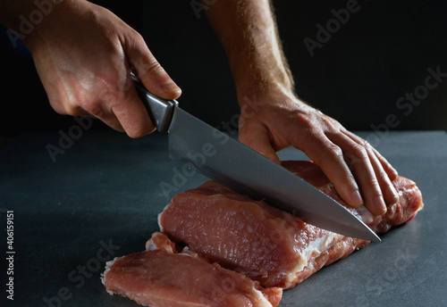 The chef is cutting fresh raw meat into steaks. Close-up on a gray background.