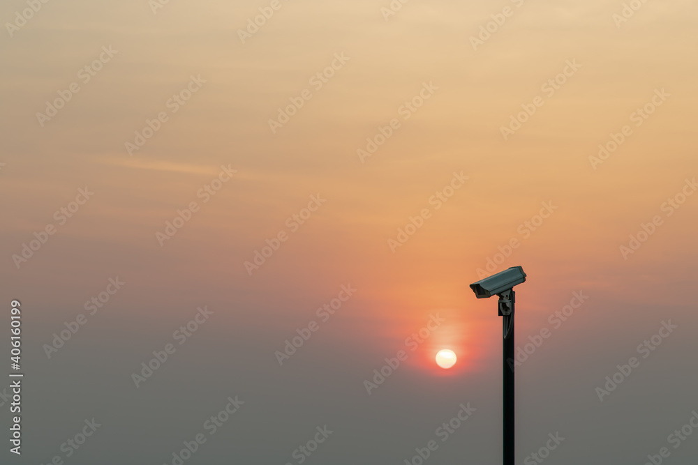 Modern surveillance camera in the foreground The orange sun shing bright before the sun was setting. The concept of surveillance evening time, copy space, Selective focus. Modern surveillance camera in the foreground The orange sun shing bright before the sun was setting. The concept of surveillance evening time, copy space, Selective focus.