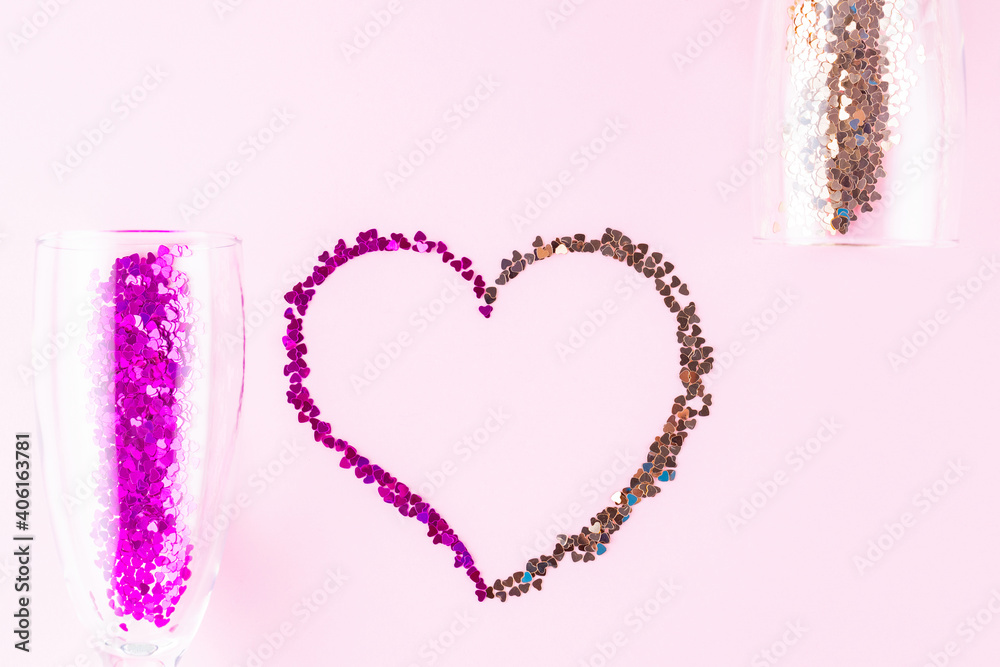 Heart shape made of multicolored glitter. Two champagne glasses with splash of heart shaped confetti over pink background. Valentine's Day concept. Flat lay