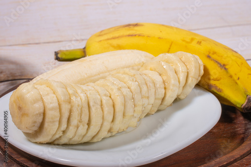 Sliced banana on a white plate on a wooden tray with another banana in the background