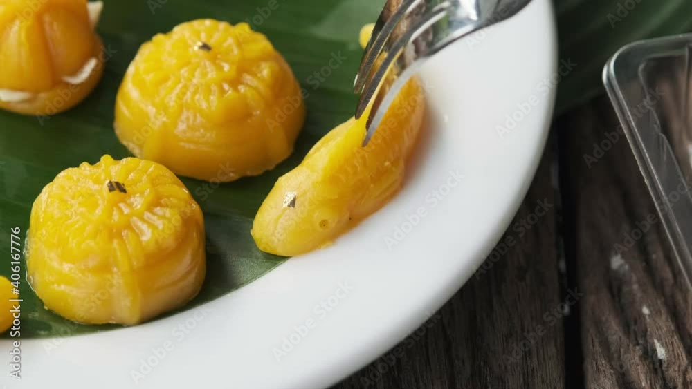 Fork is dipping into the dessert Thong-Eek, Sane Chan and Kanom Jamongkut (Thai sweets) on a white plate with banana leaves. Fork is dipping into the dessert Thong-Eek, Sane Chan and Kanom Jamongkut (Thai sweets) on a white plate with banana leaves.