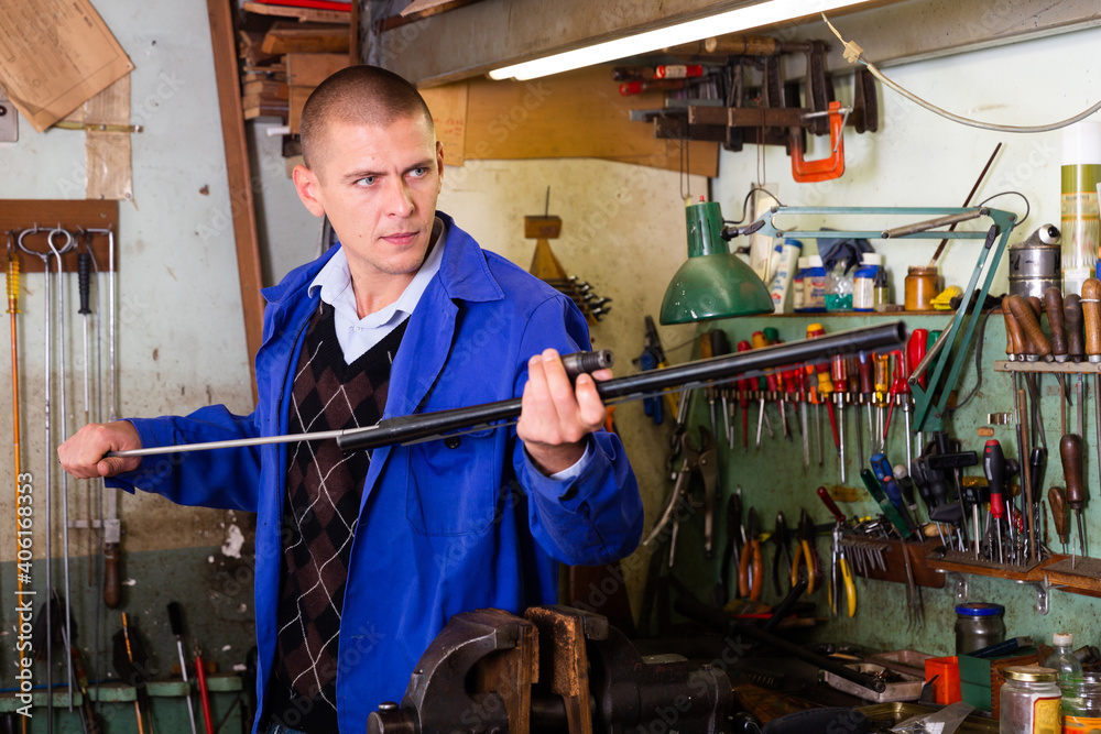 Professional gun repairman performing cleaning shotgun barrel before assembly in workshop .