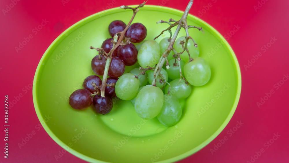 Fresh red and green grapes in a bowl isolated on pink background. Selective focus on the fresh red grapes Fresh red and green grapes in a bowl isolated on pink background. Selective focus on the fresh red grapes
