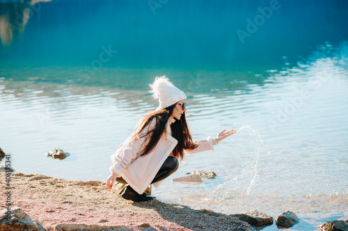 Lovely girl makes splashes of water from a mountain lake. Winter vacation, Bavaria.