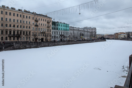 Old houses stand on the embankment of a small river in the city. Frozen river in winter. It's a nasty day.  © Kooper
