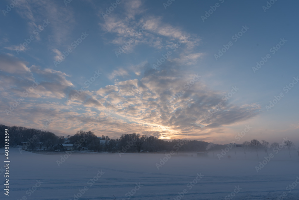 Sonnenuntergang  auf dem Land  b ei Nebel und Schnee im Winter  mit Feld, Wald,  Wolken