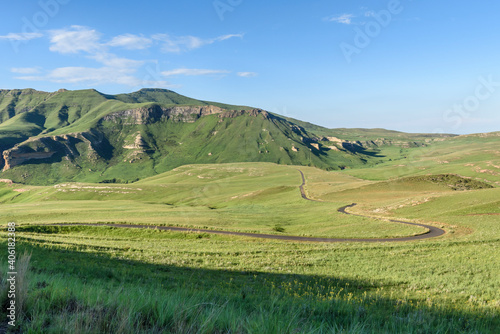 Winding scenic road through a green field grass landscape in mountain scenery with clouds in the sky