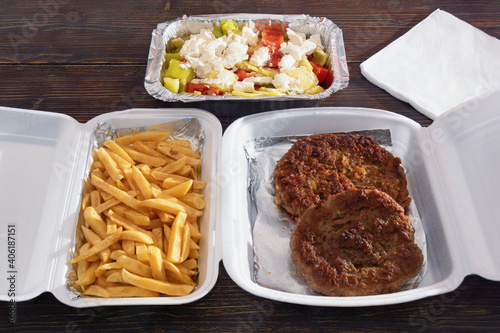 Food delivery. Balkan cuisine. Pljeskavica - grilled dish of minced meat;  french fries and salad in takeaway containers on rustic wooden table