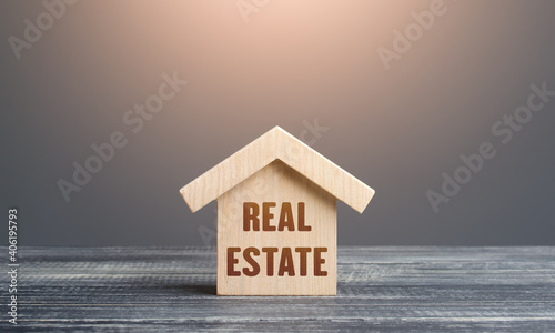 Wooden figurine of a house with word Real Estate. Buying and selling. Housing, realtor services. Construction industry, building maintenance. Mortgage loan. Assets and tax payments. Stamp duty