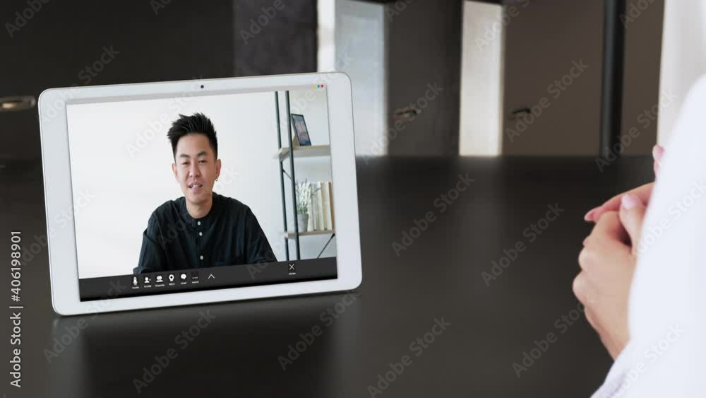 Video conference. Internet meeting. Business telecommuting. Remote discussion. Asian male CEO on tablet screen listening to female partner speaking at modern home office workplace. Video conference. Internet meeting. Business telecommuting. Remote discussion. Asian male CEO on tablet screen listening to female partner speaking at modern home office workplace.