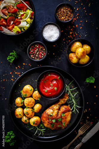 Barbecue chicken drumsticks with baked potatoes on black wooden table