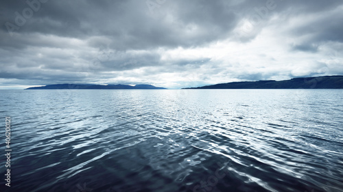 Fototapeta Naklejka Na Ścianę i Meble -  Panoramic view of the rocky river shores from the water. Trees, hills and mountains in the background. Cloudy blue sky. Gare Loch, Firth of Clyde, Scotland, UK
