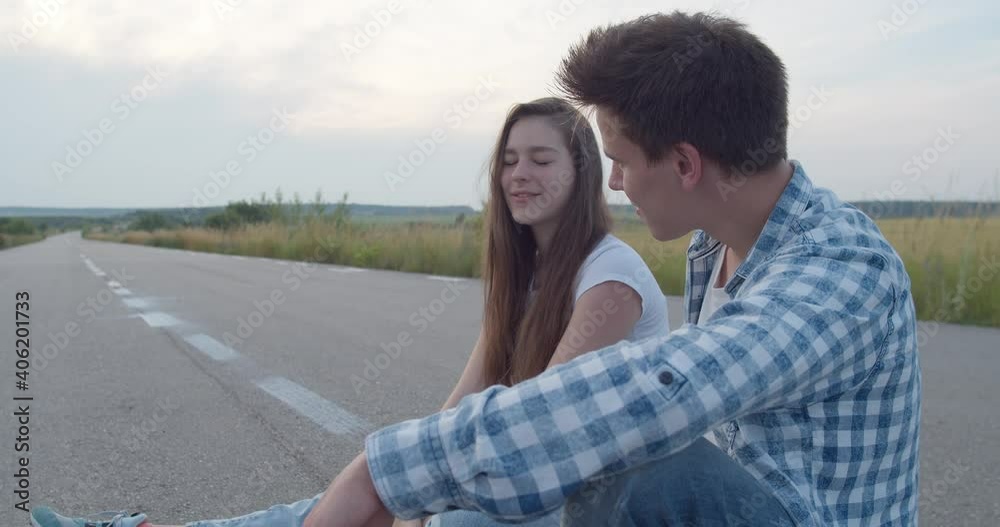 Millennial teens sitting on skateboard at camera and having joy during a talk Millennial teens sitting on skateboard at camera and having joy during a talk
