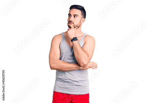 Young handsome man wearing swimwear and sleeveless t-shirt with hand on chin thinking about question, pensive expression. smiling with thoughtful face. doubt concept.