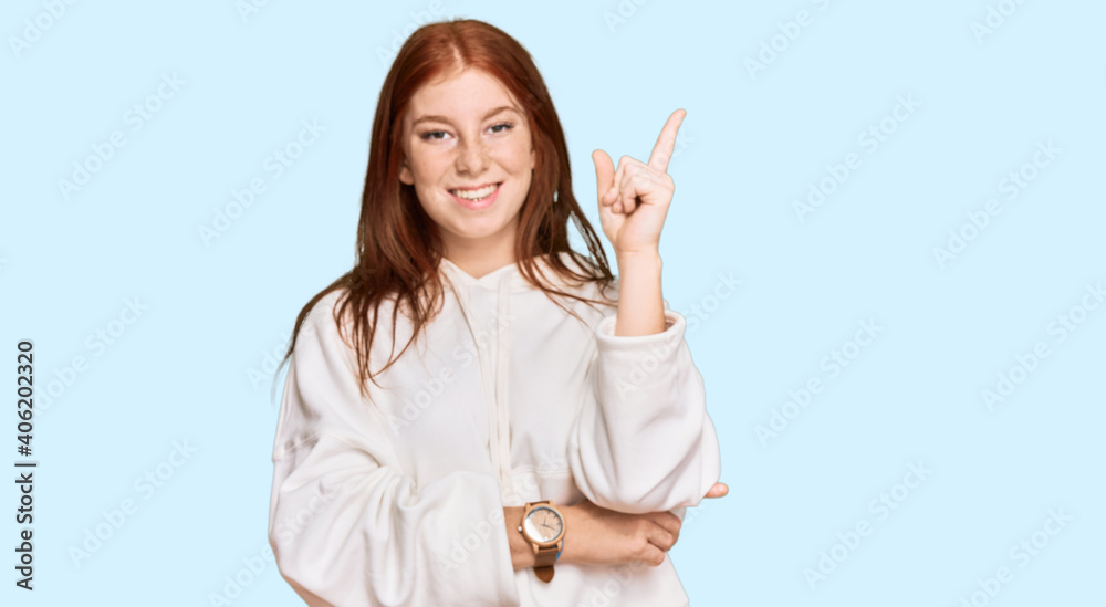 Young read head woman wearing casual sweatshirt smiling happy pointing with hand and finger to the side Young read head woman wearing casual sweatshirt smiling happy pointing with hand and finger to the side