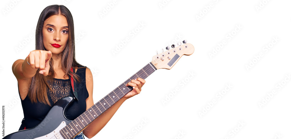 Young hispanic woman playing electric guitar pointing with finger to the camera and to you, confident gesture looking serious