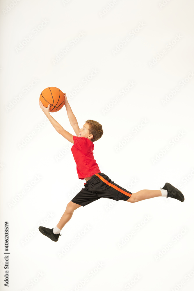 Adorable sporty boy holding basketball ball and jumping
