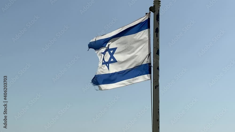 Partially torn israeli flag is waving in the wind against blue sky background. 4K