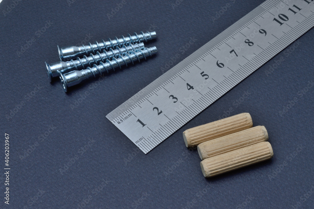 furniture screw, ruler and wooden dowel lie on a dark background. close-up.