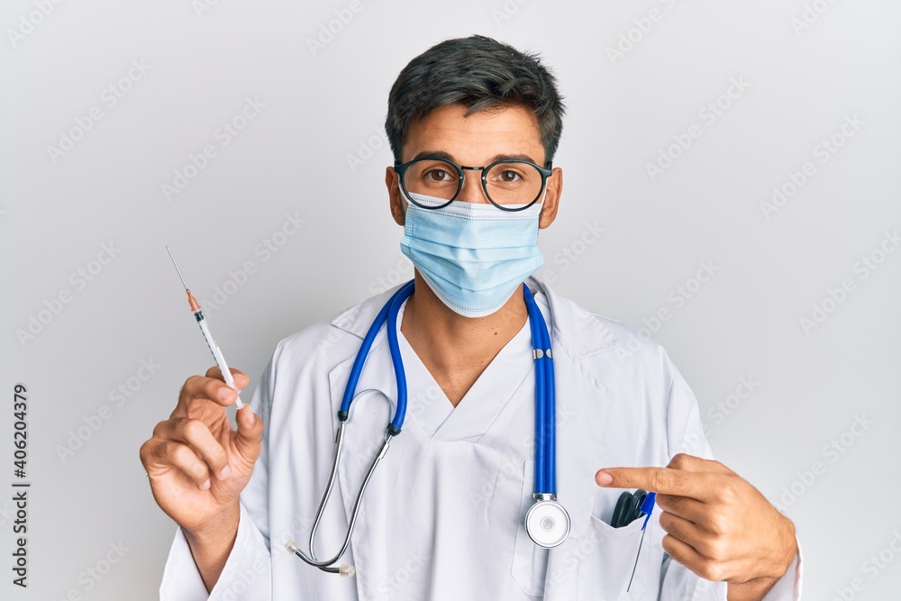 Young handsome man wearing doctor uniform and medical mask holding syringe pointing finger to one self smiling happy and proud