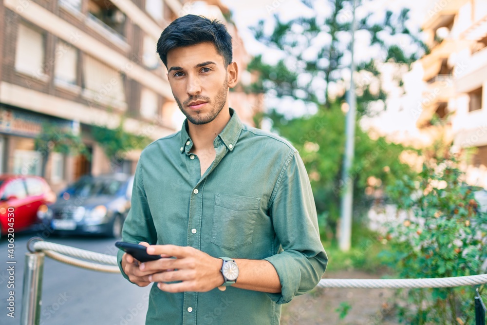 Young latin man with serious expression using smartphone walking at the city. Young latin man with serious expression using smartphone walking at the city.