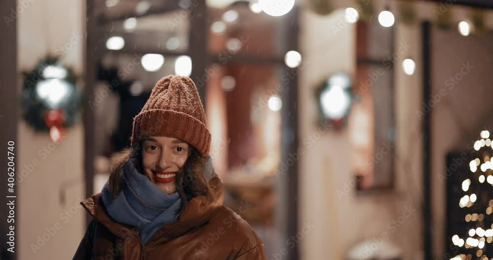 Portrait of a young enthusiastic woman on the backyard of her Christmas decorated house during a snowfall. Handheld slow video Portrait of a young enthusiastic woman on the backyard of her Christmas decorated house during a snowfall. Handheld slow video