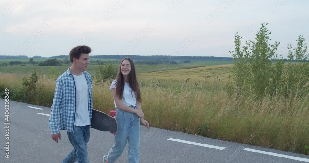 Two joyful friends walking with skateboard on road and having small talk Two joyful friends walking with skateboard on road and having small talk