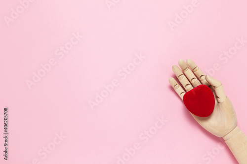 Wooden hand holds red small velvet heart shaped box for jewelry on pink background, copy space, flat lay. March 8, February 14, birthday, Valentine's, Mother's, Women's day celebration concept