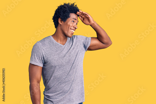 Handsome african american man with afro hair wearing casual clothes very happy and smiling looking far away with hand over head. searching concept.