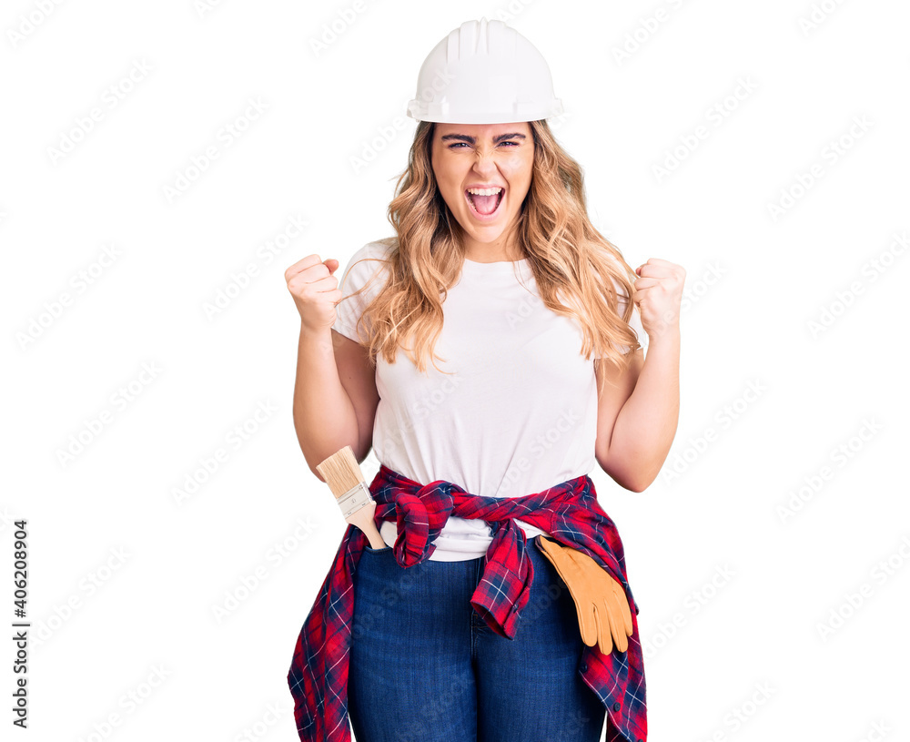 Young caucasian woman wearing security helmet celebrating surprised and amazed for success with arms raised and open eyes. winner concept. Young caucasian woman wearing security helmet celebrating surprised and amazed for success with arms raised and open eyes. winner concept.