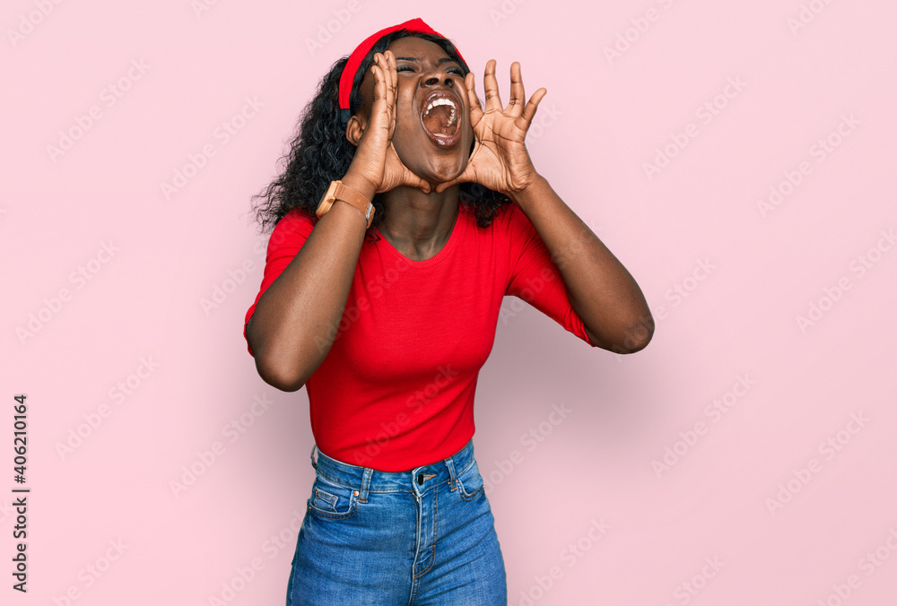 Beautiful african young woman wearing casual clothes shouting angry out loud with hands over mouth Beautiful african young woman wearing casual clothes shouting angry out loud with hands over mouth