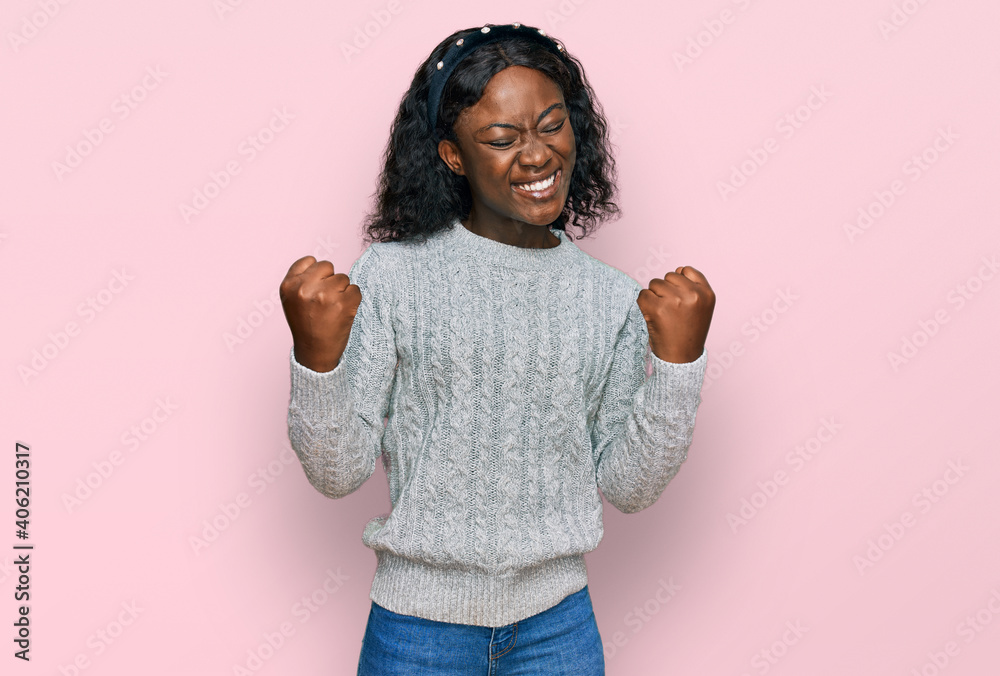 Beautiful african young woman wearing casual winter sweater excited for success with arms raised and eyes closed celebrating victory smiling. winner concept. Beautiful african young woman wearing casual winter sweater excited for success with arms raised and eyes closed celebrating victory smiling. winner concept.
