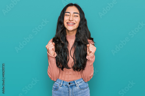 Hispanic teenager girl with dental braces wearing casual clothes celebrating surprised and amazed for success with arms raised and open eyes. winner concept. © Krakenimages.com