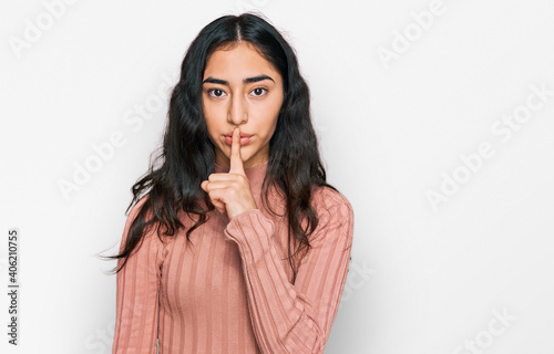 Hispanic teenager girl with dental braces wearing casual clothes asking to be quiet with finger on lips. silence and secret concept.