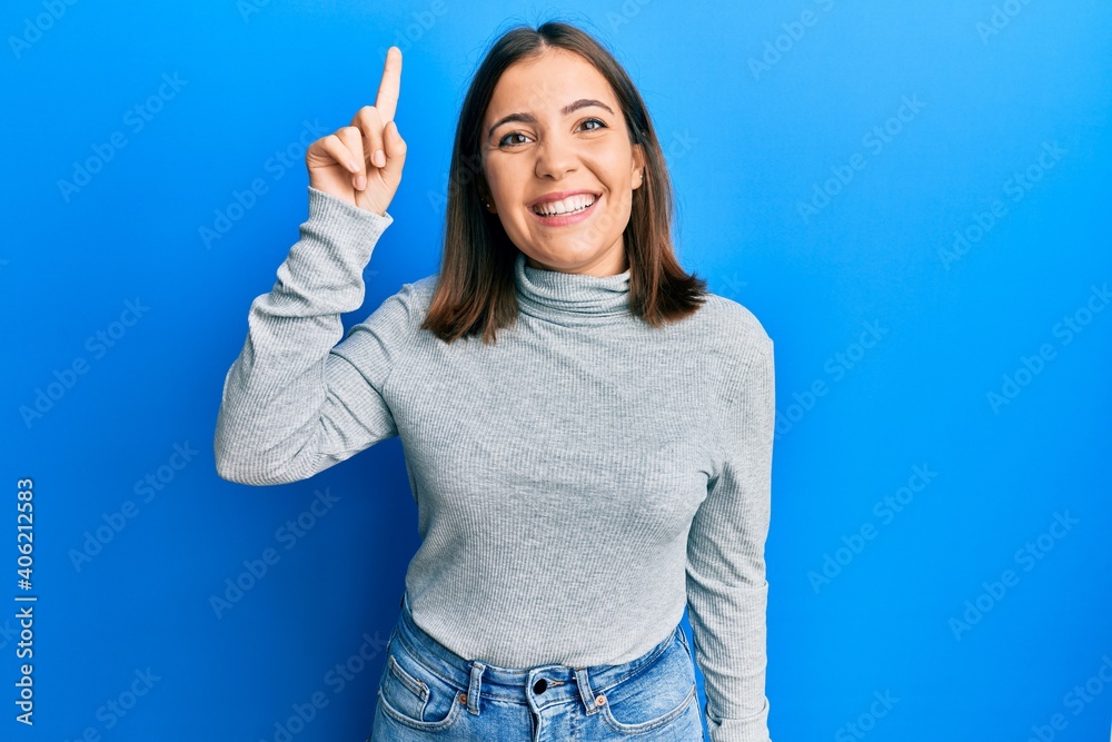 Young beautiful woman wearing casual turtleneck sweater pointing finger up with successful idea. exited and happy. number one. Young beautiful woman wearing casual turtleneck sweater pointing finger up with successful idea. exited and happy. number one.