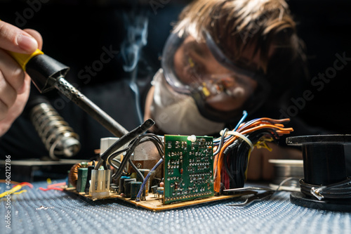 Bilde på lerret A man in glasses and a mask, with a soldering iron, repairs equipment
