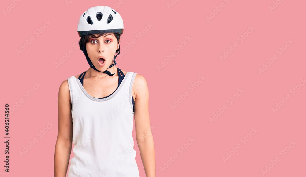 Beautiful young woman with short hair wearing bike helmet scared and amazed with open mouth for surprise, disbelief face Beautiful young woman with short hair wearing bike helmet scared and amazed with open mouth for surprise, disbelief face