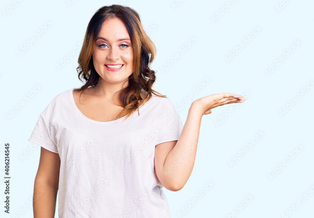 Young beautiful caucasian woman wearing casual white tshirt smiling cheerful presenting and pointing with palm of hand looking at the camera. Young beautiful caucasian woman wearing casual white tshirt smiling cheerful presenting and pointing with palm of hand looking at the camera.