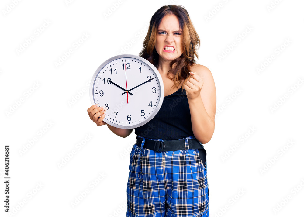 Young beautiful caucasian woman holding big clock annoyed and frustrated shouting with anger, yelling crazy with anger and hand raised