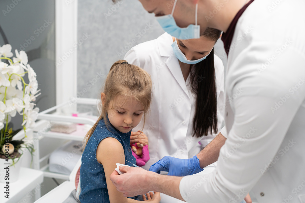 The doctor is getting ready to vaccinate a little girl. A young nurse sits next to the child to make the child feel safe. Preventive vaccine for young children. The doctor is getting ready to vaccinate a little girl. A young nurse sits next to the child to make the child feel safe. Preventive vaccine for young children.