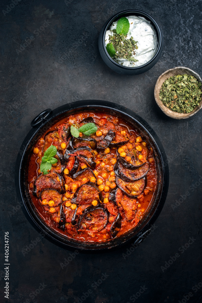 Modern style slow cooked Lebanese vegetarian eggplant stew maghmour served with chickpeas and yoghurt as top view in a design pot with copy space