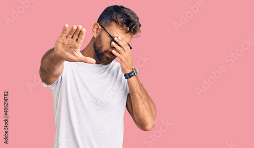 Young hispanic man wearing casual clothes and glasses covering eyes with hands and doing stop gesture with sad and fear expression. embarrassed and negative concept.