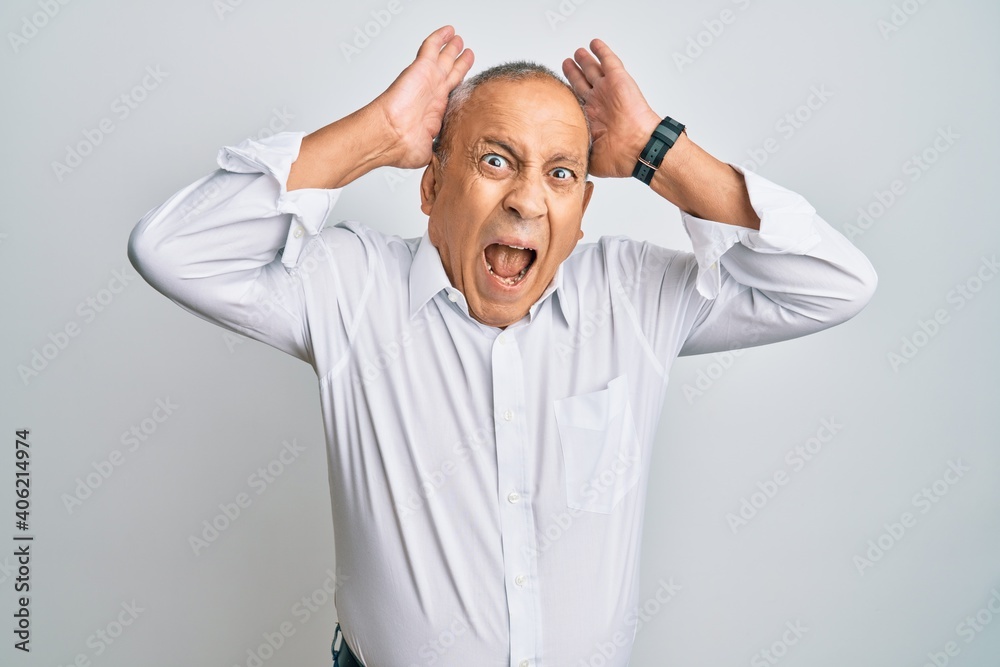 Handsome senior man wearing casual white shirt crazy and scared with hands on head, afraid and surprised of shock with open mouth