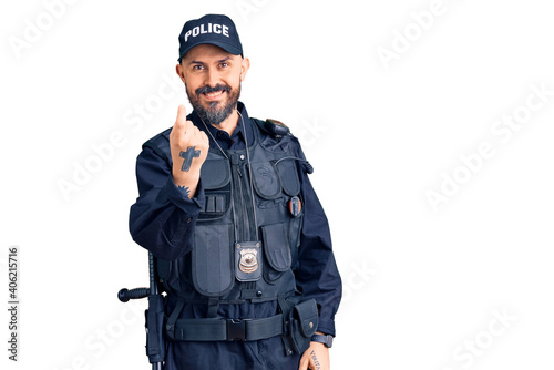 Young handsome man wearing police uniform beckoning come here gesture with hand inviting welcoming happy and smiling