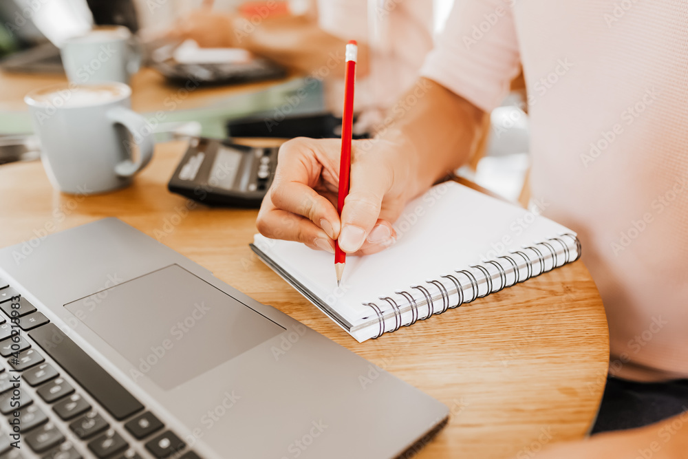 Man writes business information in notebook at workplace in office with calculator and laptop Man writes business information in notebook at workplace in office with calculator and laptop