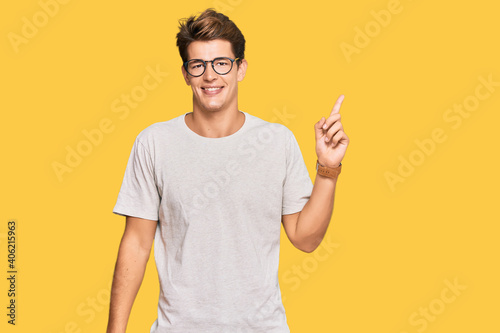 Handsome caucasian man wearing casual clothes and glasses with a big smile on face, pointing with hand finger to the side looking at the camera.