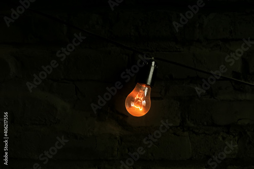 a light bulb against a dark brick wall in the loft style shines with a beautiful orange light © stalk