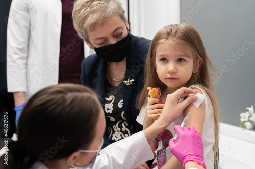 A nurse sticks a needle into the girl's arm with the new vaccine. Grandma cheers her granddaughter during the vaccination. The doctor makes the necessary injection into the child's arm. Preventive