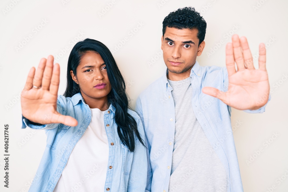 Beautiful latin young couple wearing casual clothes doing stop sing with palm of the hand. warning expression with negative and serious gesture on the face. Beautiful latin young couple wearing casual clothes doing stop sing with palm of the hand. warning expression with negative and serious gesture on the face.