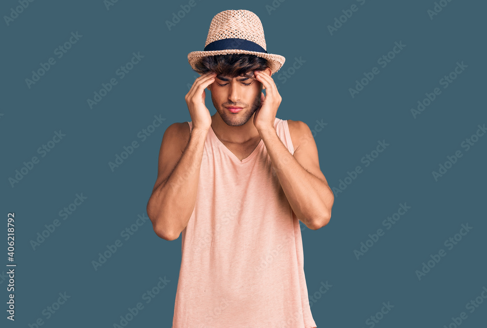 Young hispanic man wearing summer hat with hand on head for pain in head because stress. suffering migraine. Young hispanic man wearing summer hat with hand on head for pain in head because stress. suffering migraine.
